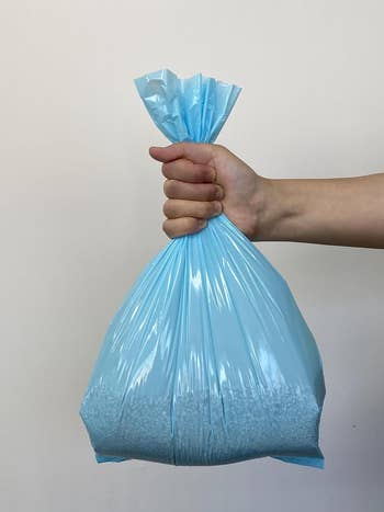 A manus  holds a sealed bluish  integrative  container  filled with tiny  achromatic  beads, suggesting a household   oregon  buying  item