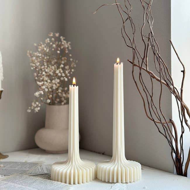 Two sculptural tapered candles with ridged bases connected a table