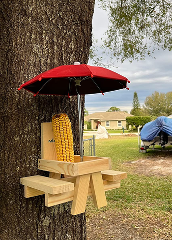a reviewer photo of the table mounted on a tree with a corn of cob standing on it 