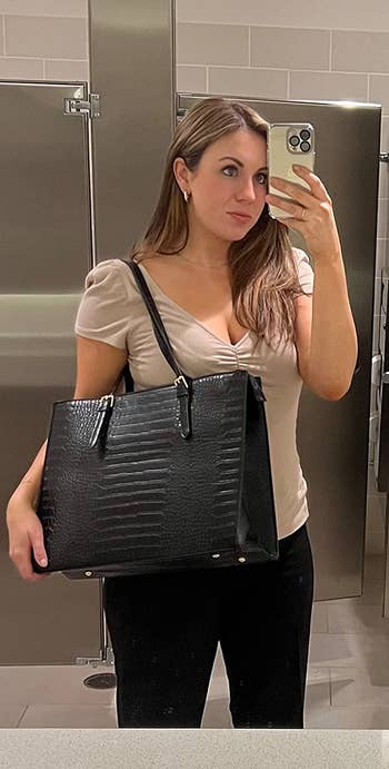 A reviewer wearing the bag in black while taking a mirror selfie in a public bathroom