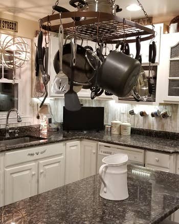 Reviewer image of hanging ceiling pot and pan organizer with pots on hooks and dishes stacked on shelf