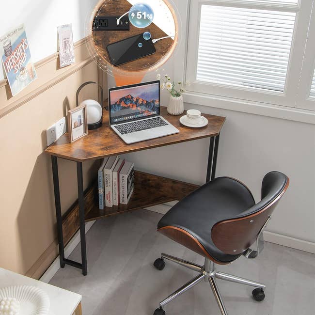 Compact corner desk setup with a laptop, lamp, books, and a cup of coffee. A cellphone charges on a wireless charging pad