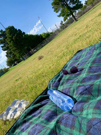 reviewer POV photo of green plaid fleece picnic blanket on the grass
