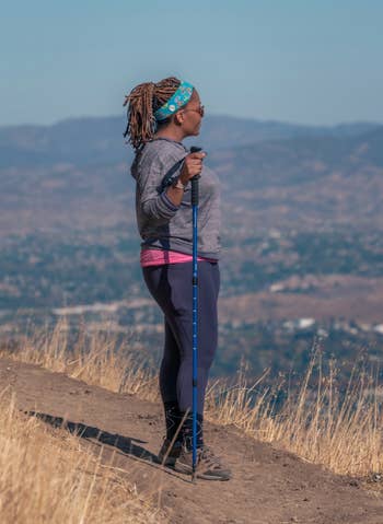 Person with trekking pole on mountain trail, wearing athletic gear, headband, and sunglasses