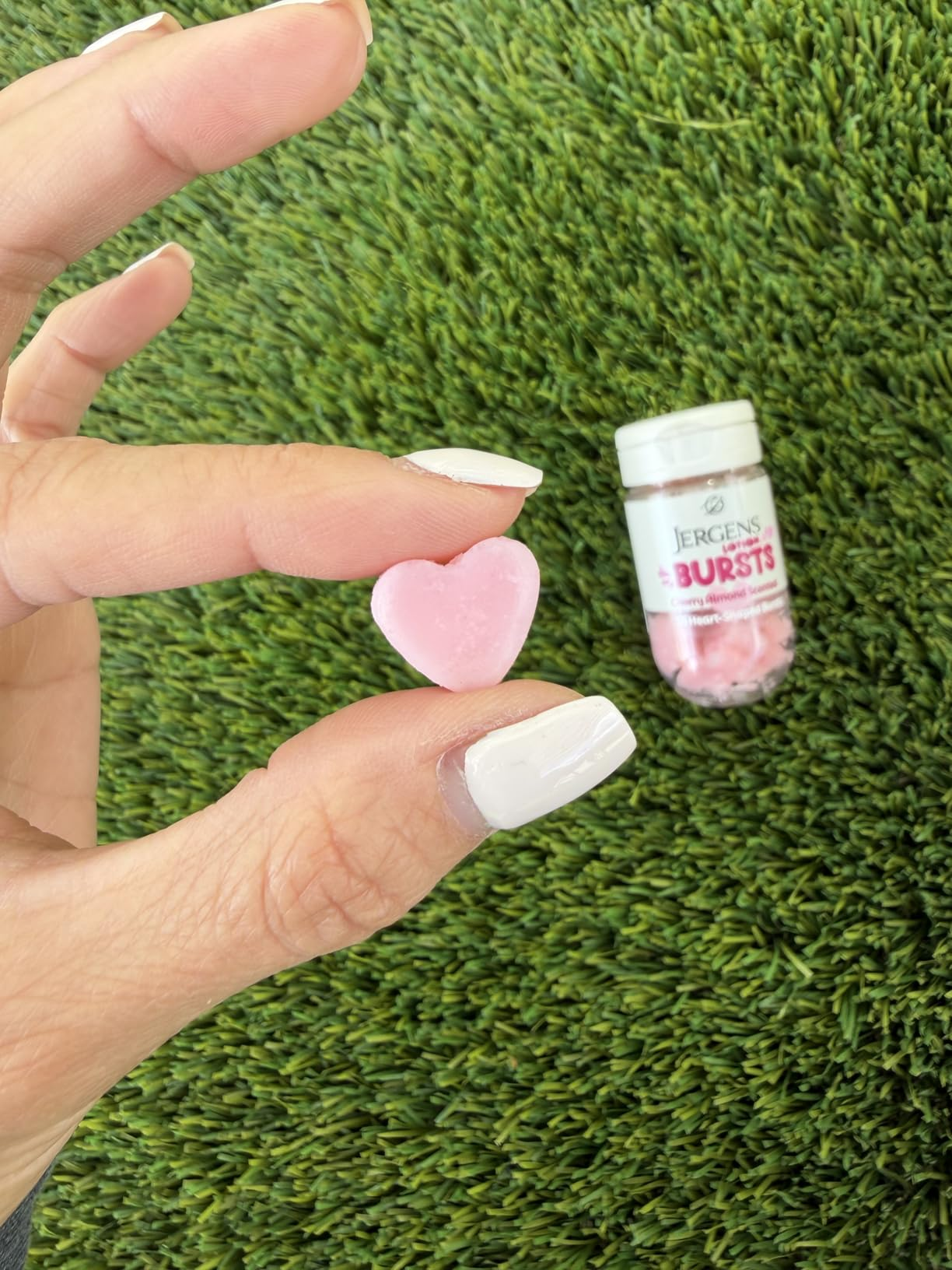 Hand holding a heart-shaped lotion burst, with a vessel  labeled 
