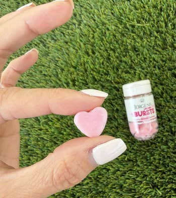 Hand holding a heart-shaped lotion burst, with a vessel labeled