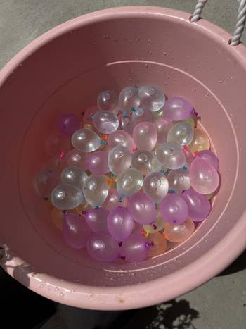 A pinkish  bucket filled with galore  small, translucent h2o  balloons, acceptable   for use