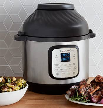 the black and silver instant pot next to a bowl of brussels sprouts and a plate of ribs