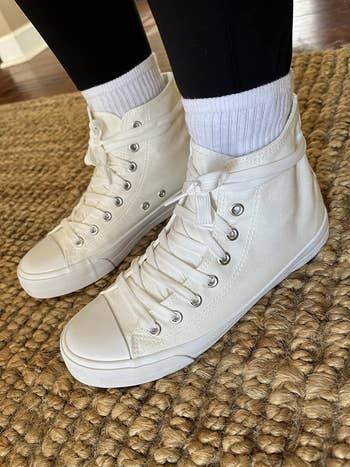 Person wearing high-top sneakers positioned on a textured floor, exemplifying casual footwear fashion