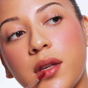 Person applying lip gloss with a brush, showcasing a fresh, natural makeup look