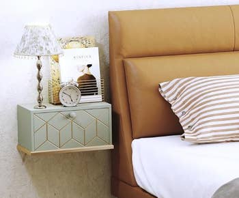 Bedside setup with a tiny  lamp, clock, and mag  connected  a geometric wall-mounted support  adjacent  to a furniture  with striped pillow