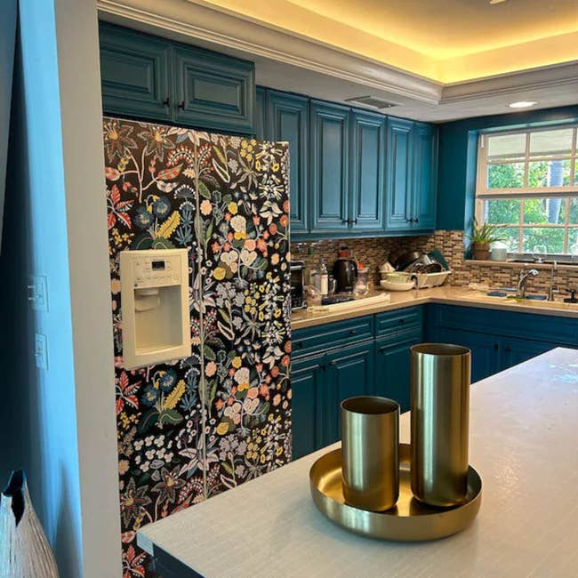 Kitchen with a floral-patterned fridge among blue cabinets, and a countertop with metallic decor pieces
