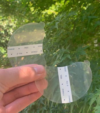 A manus holds wide under-eye masks with peel tabs, acceptable against lush greenish foliage background