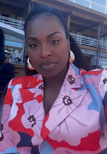 Person wearing a floral-patterned blouse with ample hoop earrings, posing outdoors