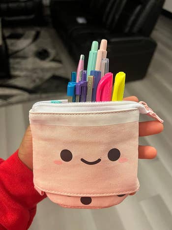 Person holding the pencil case with the top pulled down to reveal stationery inside
