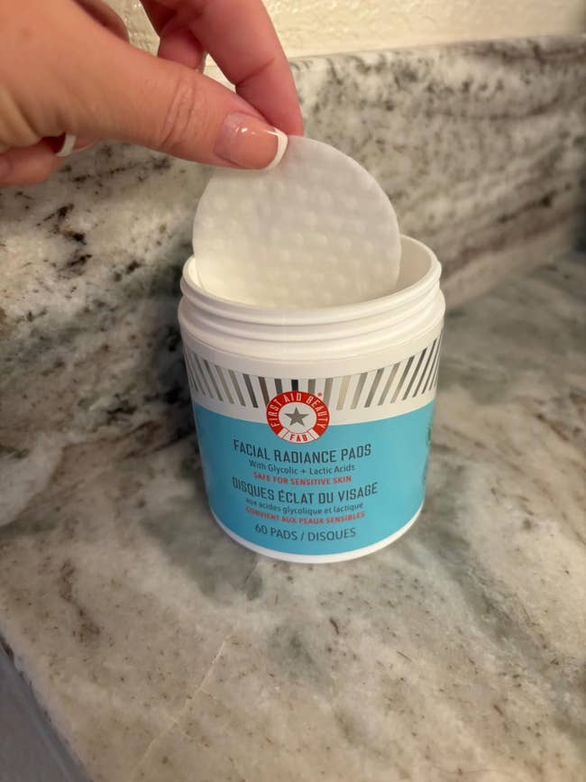 A manus holds a facial radiance pad supra an unfastened jar labeled