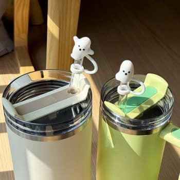 Two insulated travel mugs with ghost-themed straw caps on straws