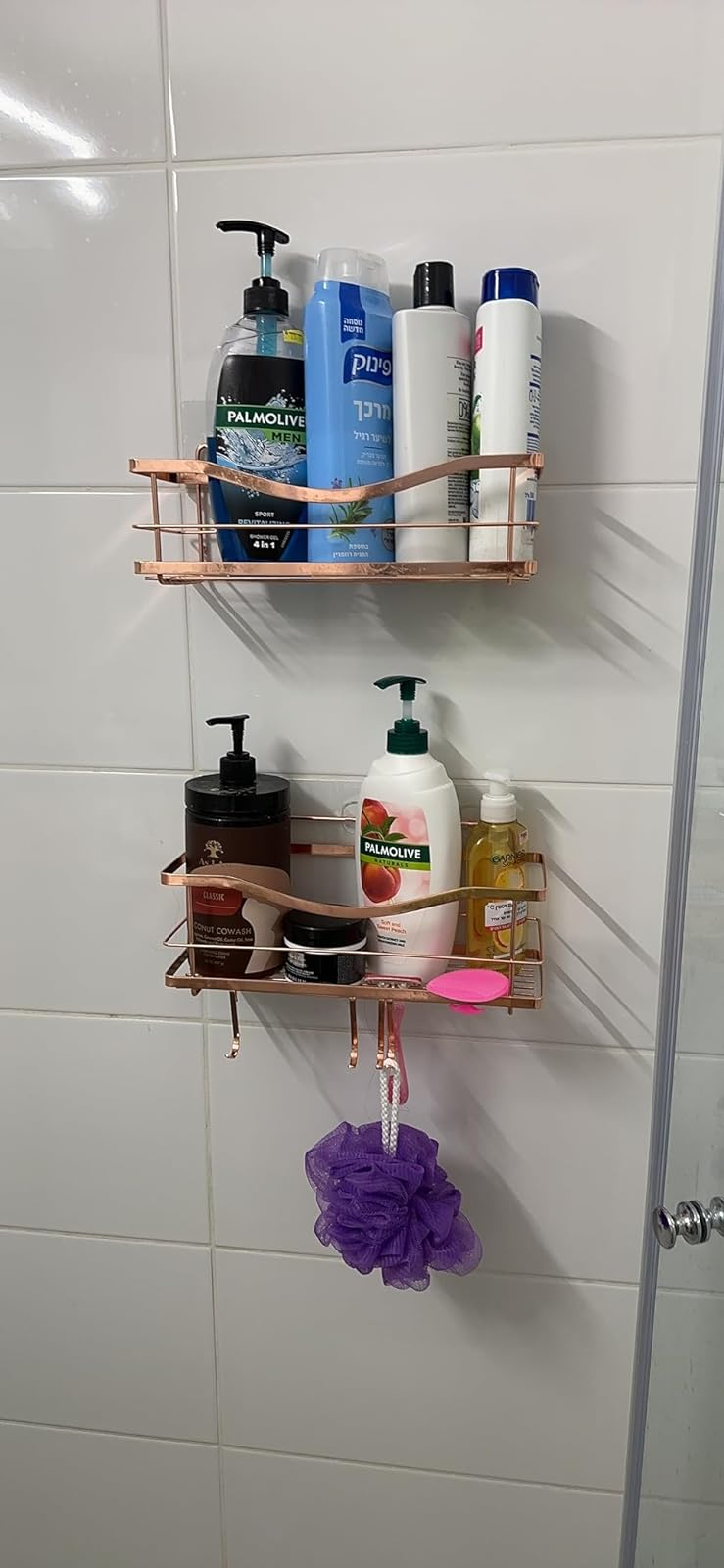 Reviewer's shower wall with two rose gold shower caddies with various toiletries and a purple loofah
