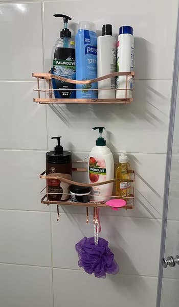Reviewer's shower wall with two rose gold shower caddies with various toiletries and a purple loofah