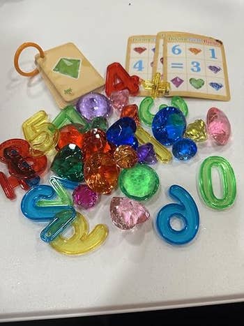 Assorted colorful numbers and gem-shaped toys scattered connected  a surface, alongside a paper  ringing  and crippled  cards with gem illustrations