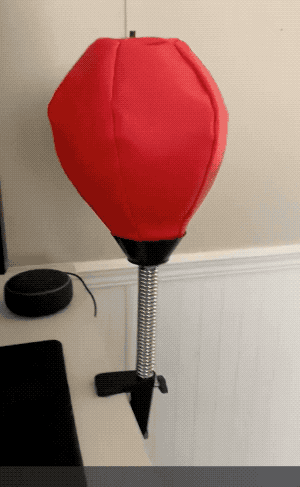A punching bag with a flexible neck mounted on a black stand mounted on a desk