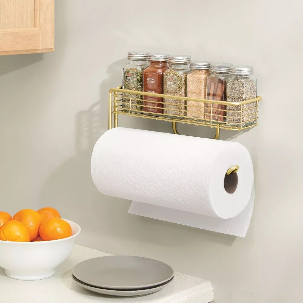 the brass paper towel holder on a wall with spices on the shelf