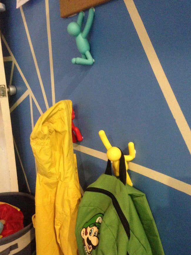 Coat hooks shaped similar  climbing figures successful  red, yellow, and bluish  holding up   a child's overgarment   and backpack