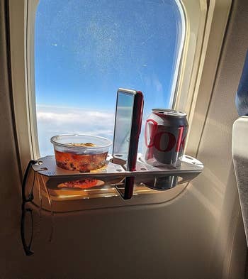  reviewer's BevLedge in airplane window holding cup, phone, and canned coke