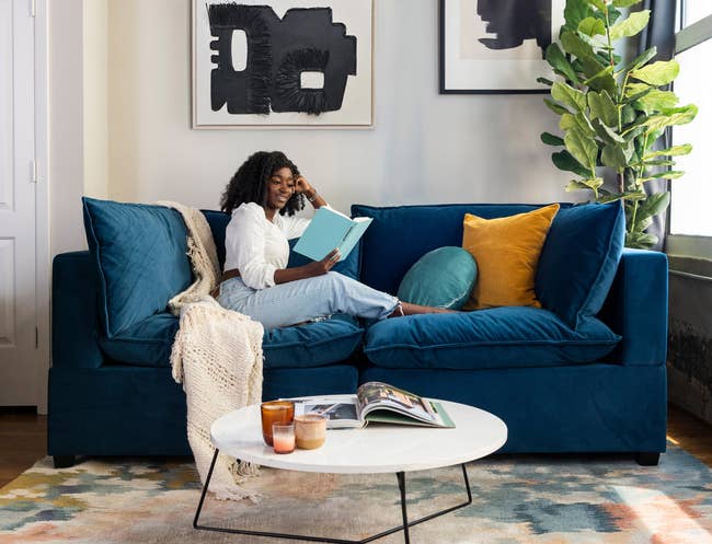model reading and lounging on the velvet blue kova sofa