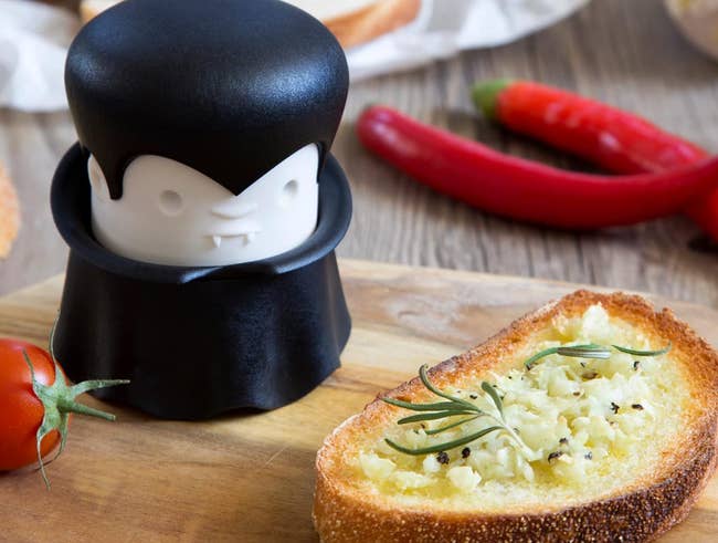 Vampire-themed garlic mincer next to toast with a lot of garlic on it