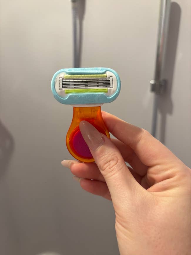 travel A hand holds a small, colorful razor in a shower, possibly highlighting its design and ease of use for shaving