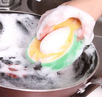 A model cleaning a pan with a soapy avocado shaped sponge 