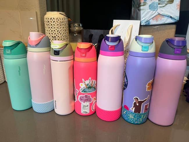 Seven water bottles with different designs, some adorned with stickers, lined up on a surface