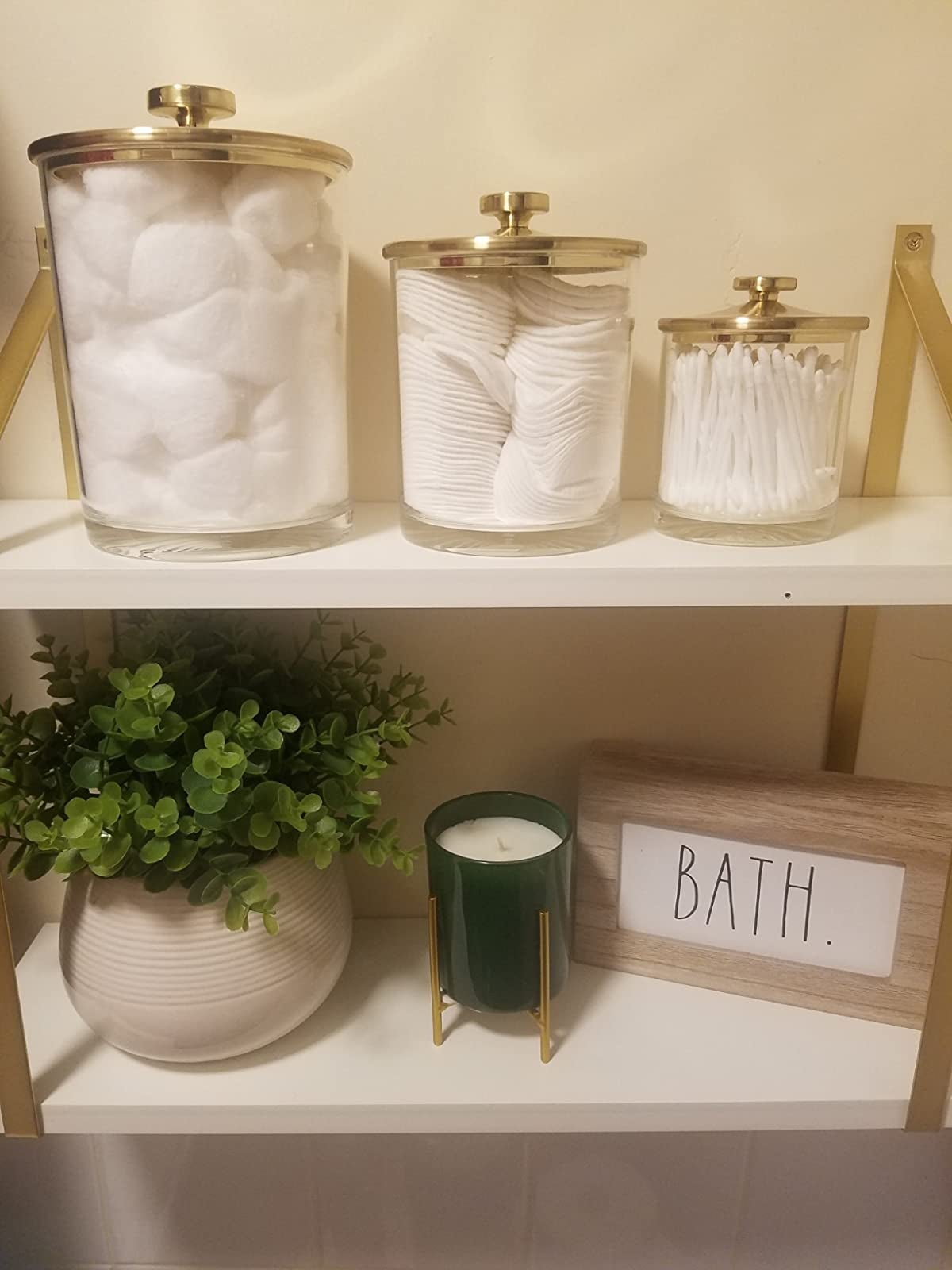 reviewer image of a large, medium, and small clear jar with a gold lid sitting on a counter with assorted bath products inside them