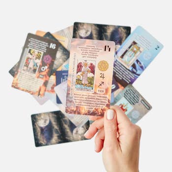 Hand holding a deck of tarot cards spread out, focusing on one card with symbolic artwork