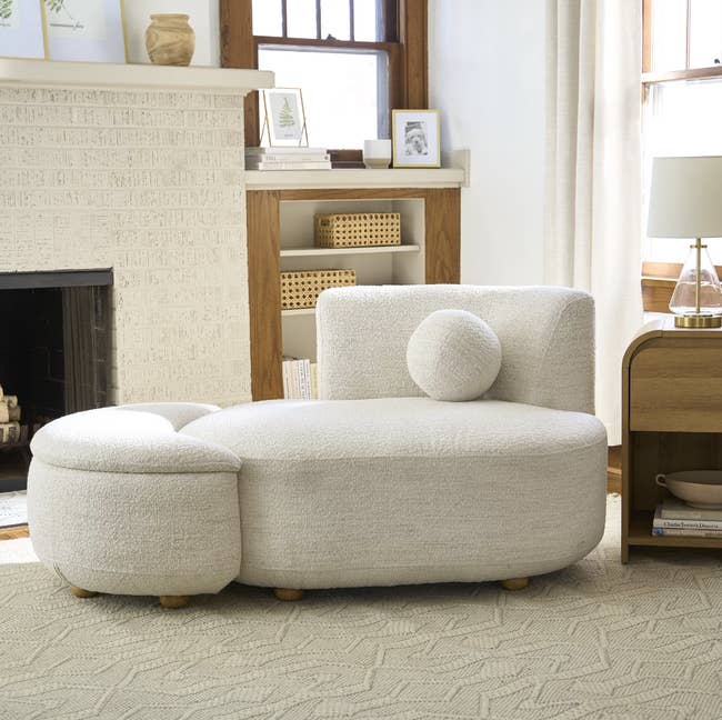 Modern achromatic sectional sofa with plush circular cushion successful a cozy surviving country setting. Fireplace and bookshelf successful the background