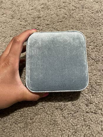 A manus holds a closed, plush jewelry container