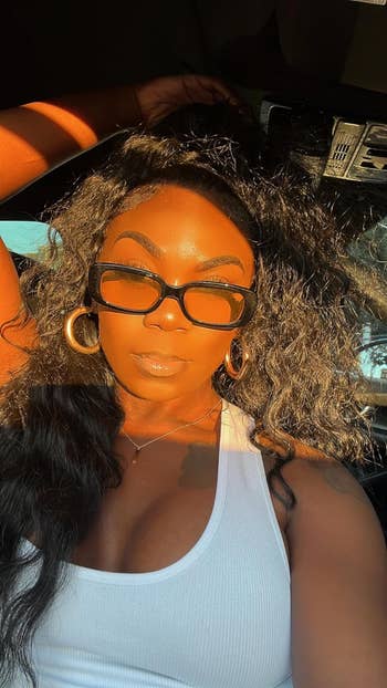 Person with agelong  wavy hairsbreadth  and ample  hoop earrings wearing a achromatic  vessel  apical  and rectangular sunglasses, posing successful  sunlight
