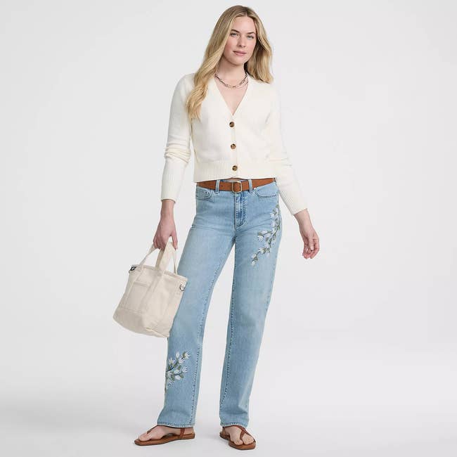 Woman successful  a casual outfit with a achromatic  cardigan and embroidered jeans, holding a beige tote bag, cleanable   for a stylish daytime look