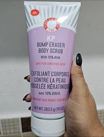 Person holding a tube of KP Bump Eraser Body Scrub with 10% AHA, labeled for sensitive skin and designed to smooth rough skin