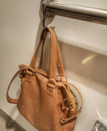 reviewer's purse hanging from the clip, which is clipped onto an arm railing in a public bathroom stall 