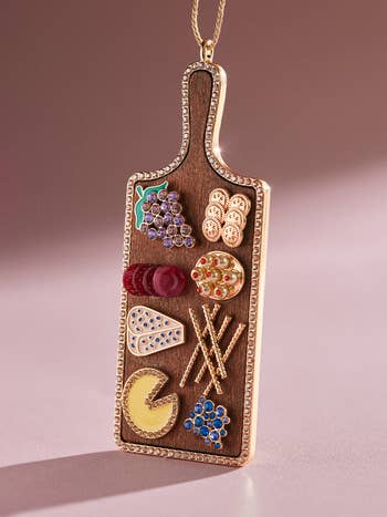 close up on the ornament that looks like a board with rhinestone and metal cheese, crackers, meat, and fruit