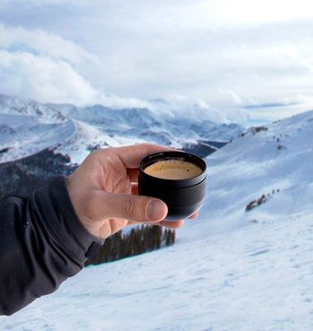 hand holding a cup of espresso on a snowy mountain