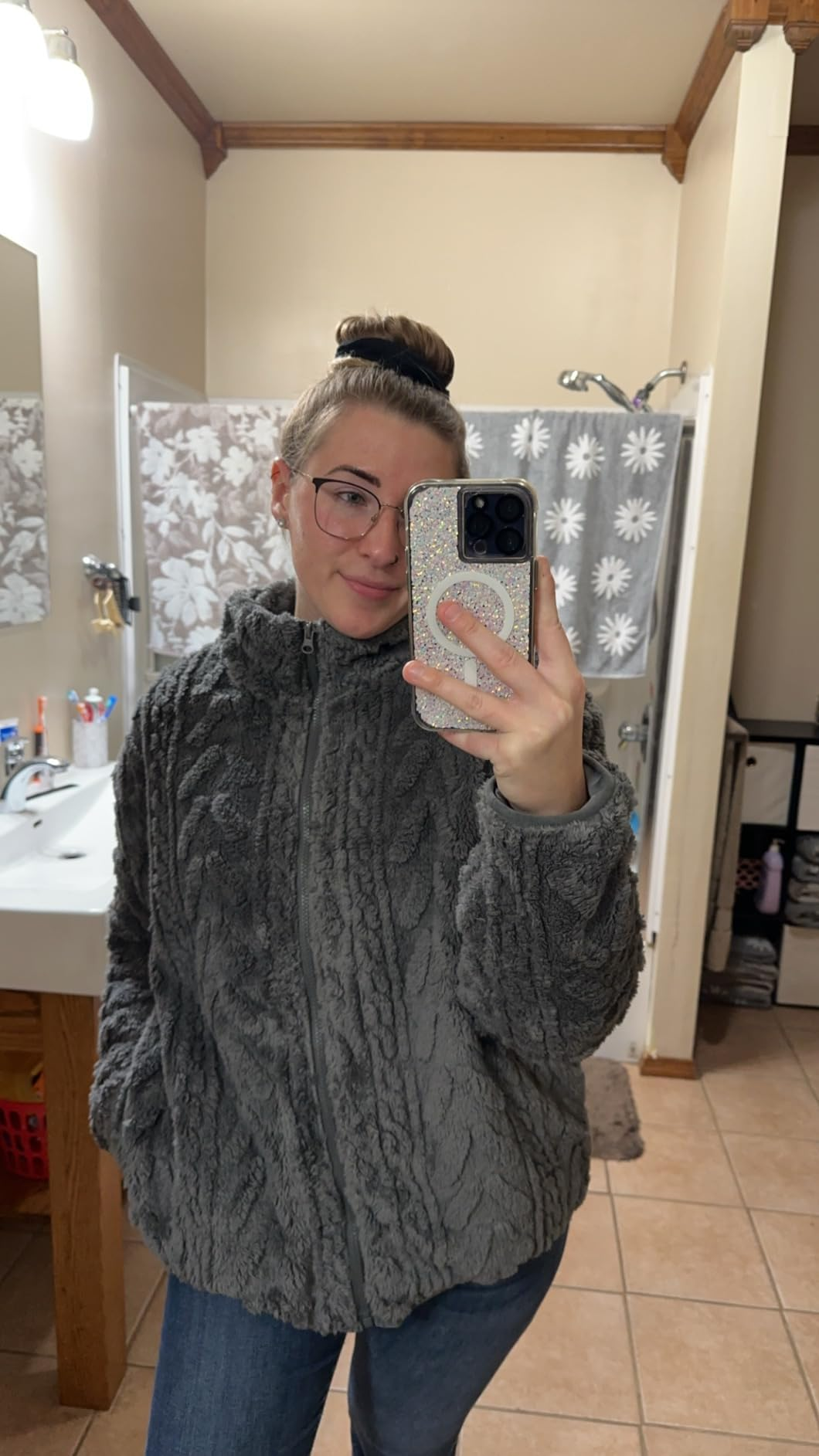 Person taking a reflector  selfie successful  a bathroom, wearing a cozy textured overgarment   with jeans, holding a sparkly telephone  case