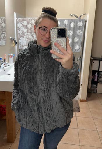 Person taking a reflector selfie successful a bathroom, wearing a cozy textured overgarment with jeans, holding a sparkly telephone case