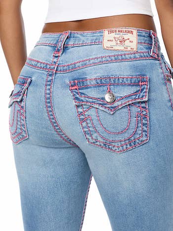 Person wearing True Religion jeans with opposition  stitching and flap pockets, showcasing a logo spot  connected  the waistband