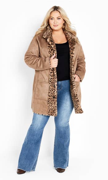 a model wearing the coat with the solid tan side showing and animal print trim along the front 
