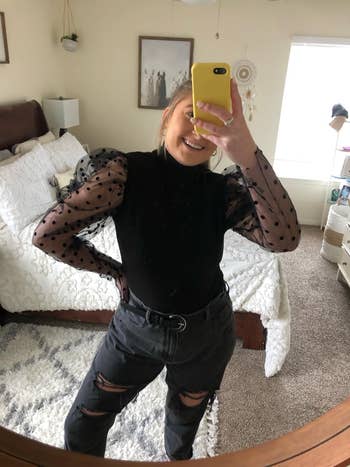 Person in a mirror selfie wearing a sheer-sleeved top and ripped jeans, possibly for a fashion look