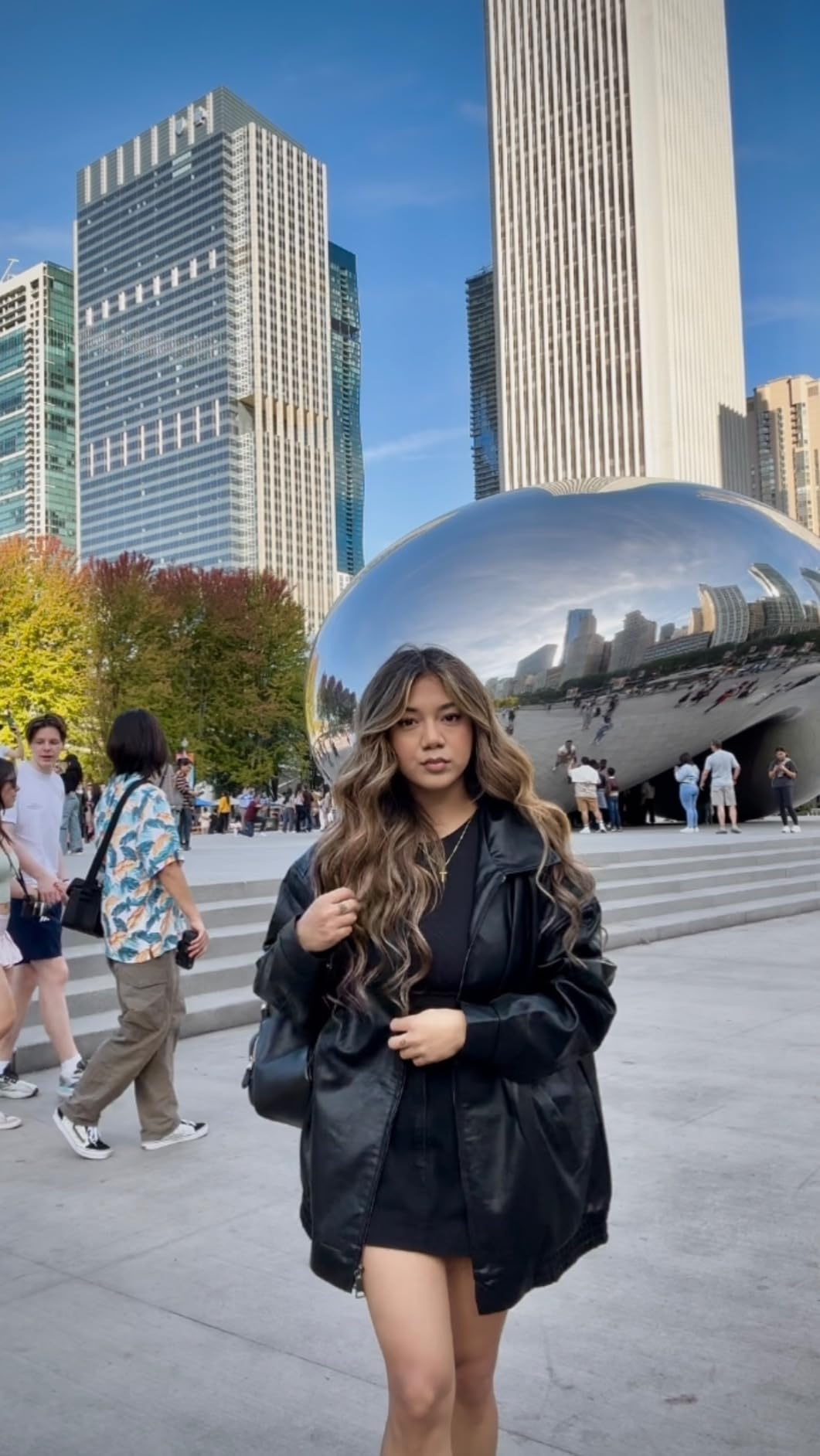 Person successful  a stylish achromatic  overgarment   poses successful  beforehand   of Chicago's Cloud Gate sculpture, with skyscrapers and radical   successful  the background