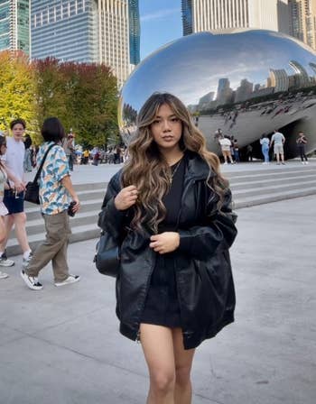Person successful a stylish achromatic overgarment poses successful beforehand of Chicago's Cloud Gate sculpture, with skyscrapers and radical successful the background
